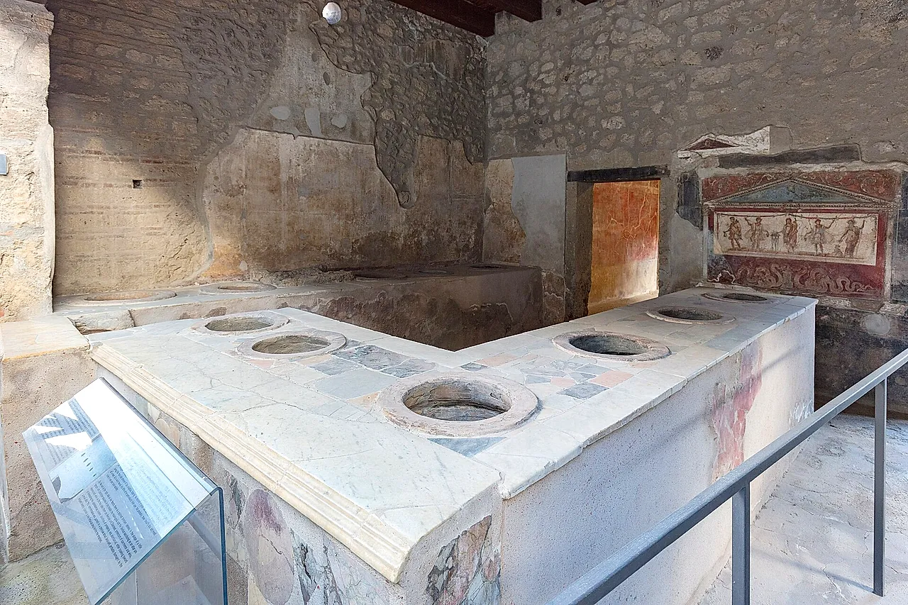 Der L-förmige Tresen des Thermopoliums des Vetutius Placidus in Pompeji, mit einem bemalten Hausaltar dahinter
