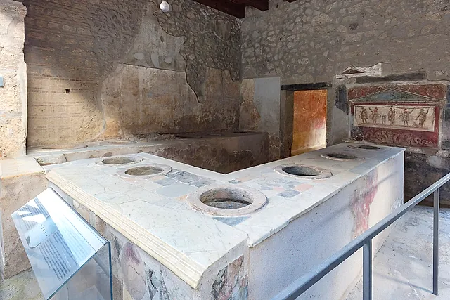 La barra en forma de L del Termopolio de Vetutius Placidus de Pompeya, con un altar pintado detrás